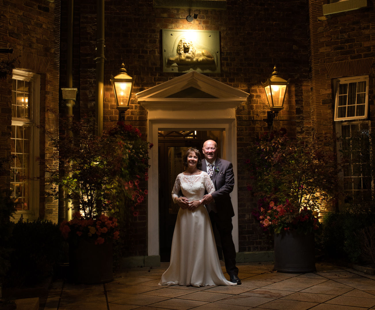 A bride and groom stand out there the entrance of the Stanneylands Hotel Winslow at night 